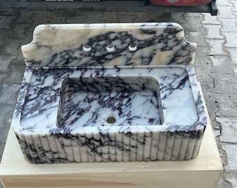 May include: A rectangular marble sink featuring a white base with prominent dark purple veining. The basin has a fluted exterior design on the front and sides, a high backsplash with three circular faucet holes, and a central drain opening.