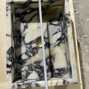 Peut inclure: Un &eacute;vier en marbre blanc avec des veines noires et violettes. L'&eacute;vier est rectangulaire et mesure 91,44 cm sur 132,08 cm. L'&eacute;vier a un drain en laiton.