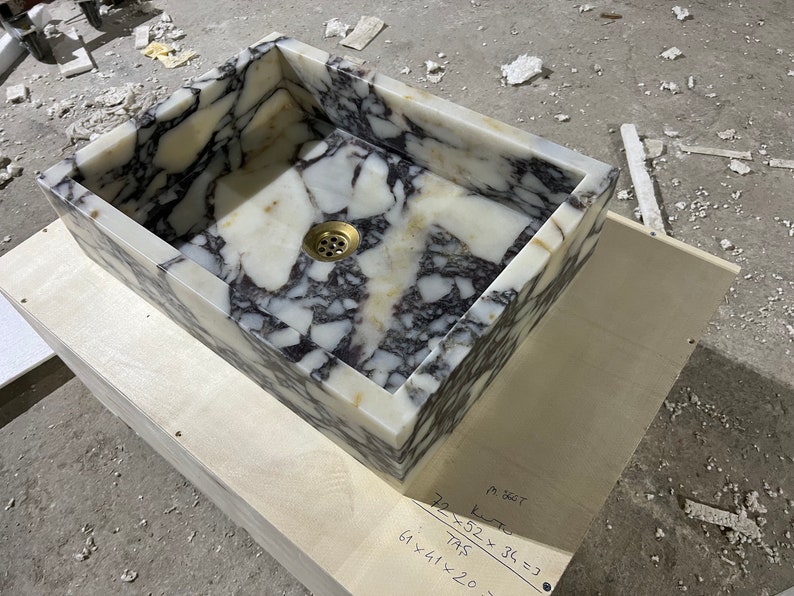 Peut inclure: Un &eacute;vier rectangulaire en marbre blanc avec des veines noires. L'&eacute;vier est dot&eacute; d'un drain en laiton. L'&eacute;vier est pos&eacute; sur une base en bois avec des mesures manuscrites en pouces.