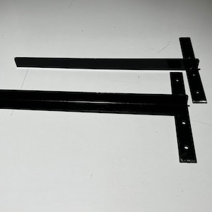 Puede incluir: Dos soportes de estante de metal negro con un diseño plano y en ángulo. Los soportes tienen varios agujeros para montaje.