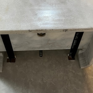 May include: A white marble sink with two black metal supports underneath. The sink is mounted on a wall and has a drain hole in the centre.
