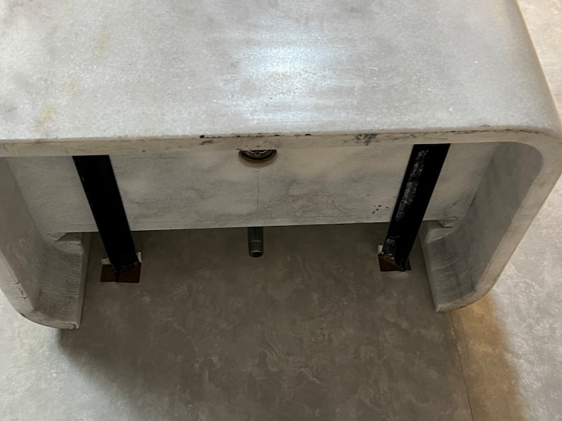 May include: A white marble sink with two black metal supports underneath. The sink is mounted on a wall and has a drain hole in the centre.
