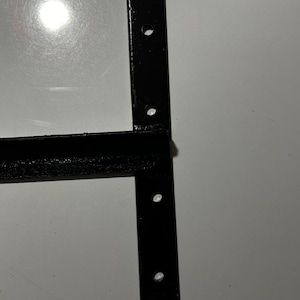 May include: Black metal bracket with four holes for mounting. The bracket has a T-shape with a long horizontal arm and a shorter vertical arm.