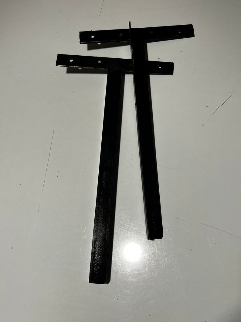 May include: Two black metal brackets with holes for screws. The brackets are L-shaped and have a flat surface on one side.