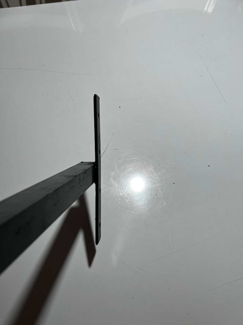 May include: Black metal shelf bracket with a rectangular shape and four holes for mounting.