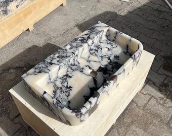 May include: Double sink bathroom vanity made of white marble with black and purple veining. The sink is sitting on a wooden base.