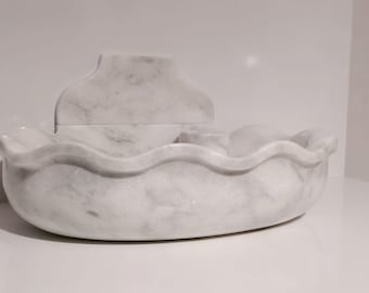 Pode incluir: Uma escultura de barco de mármore branco com uma borda ondulada. O barco tem uma seção retangular elevada na parte de trás.