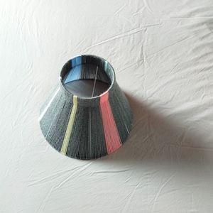 May include: A black lampshade with colorful stripes of blue, yellow, and pink.