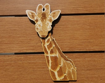 May include: A wooden cutout of a giraffe's head and neck, with a brown and tan patterned design. The giraffe is looking directly at the camera.