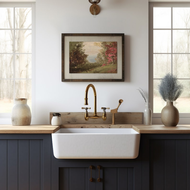 May include: A farmhouse kitchen with a white farmhouse sink and a gold faucet. The sink is set into a wooden countertop with a wooden backsplash. There is a framed landscape painting above the sink.