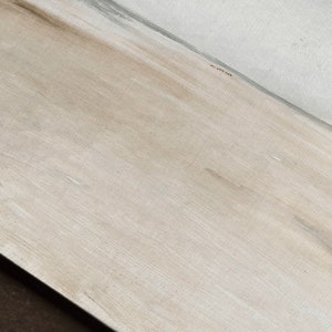 May include: A close-up of a light brown wood surface with a subtle grain pattern. The surface is smooth and appears to be lightly sanded.