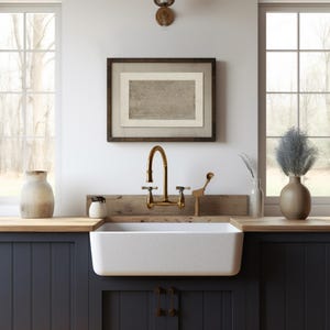 May include: A white farmhouse kitchen sink with a gold faucet and a wooden countertop. The sink is set against dark blue cabinets with a wood paneling design.