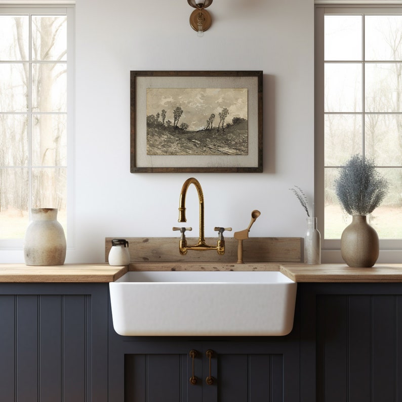 May include: A farmhouse kitchen sink with a brass faucet and a wooden countertop. A framed black and white landscape print hangs on the wall above the sink.