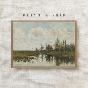 May include: A framed print of a landscape painting depicting a river flowing through a field with trees and a cloudy sky. The painting is in a light brown frame.