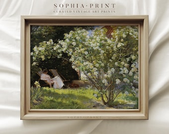 May include: A vintage painting of a woman sitting in a chair in a garden with a white flowering bush in the foreground. The painting is framed in a light wood frame.