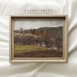 May include: A framed vintage landscape art print. The artwork depicts a rural scene with a field, trees, and buildings. The print is in a light-colored wooden frame. The text "SOPHIA PRINT CURATED VINTAGE ART PRINTS" is at the top and bottom of the frame.