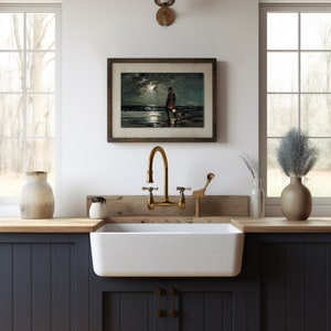 May include: A white farmhouse kitchen sink with a gold faucet and a framed black and white print of a person walking a dog on a beach at night.
