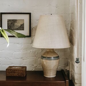May include: A ceramic table lamp with a beige and blue patterned base and a white linen lampshade. The lamp is sitting on a wooden table.