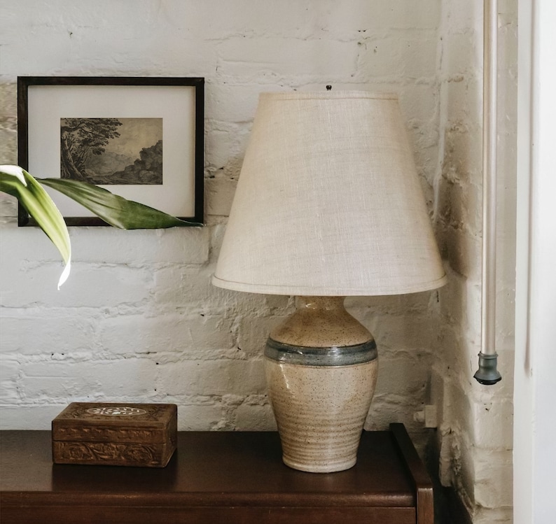May include: A ceramic table lamp with a beige and blue patterned base and a white linen lampshade. The lamp is sitting on a wooden table.