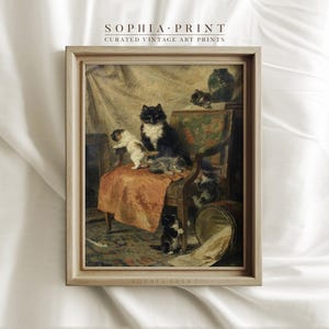 May include: A vintage painting of a black and white cat with several kittens. The cat is sitting on a chair with a red and orange cushion. The kittens are playing around the cat and chair. The painting is framed in a light wood frame.