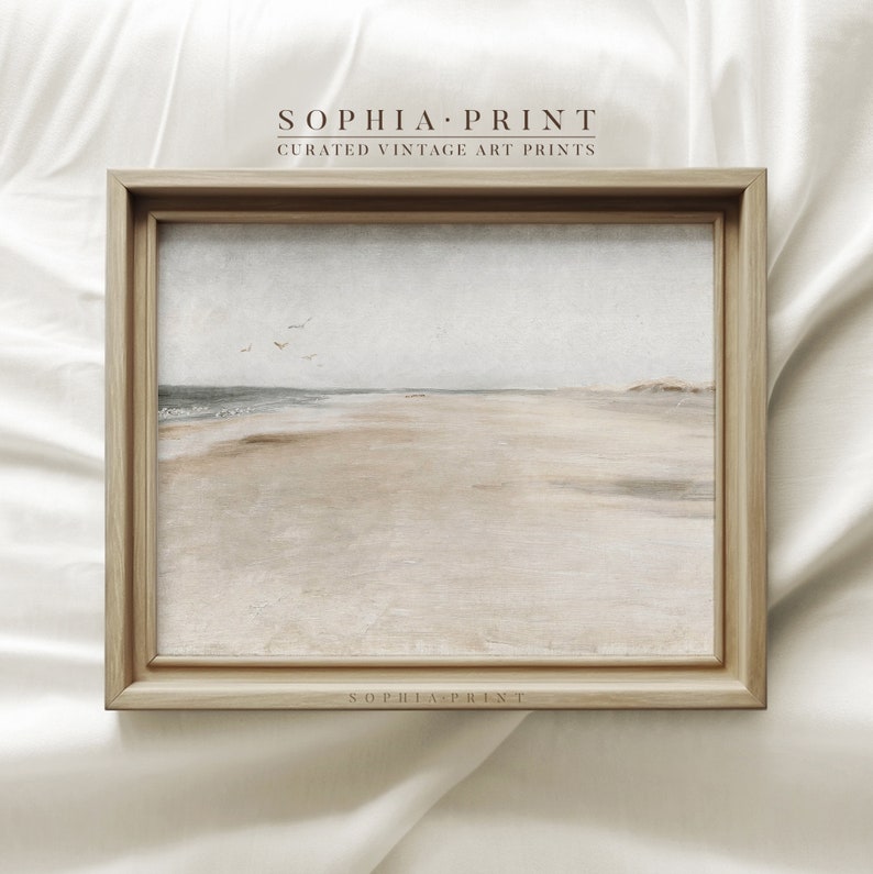 May include: A framed print of a seascape painting. The painting depicts a sandy beach with a calm ocean in the background. The sky is a light blue with a few white birds flying overhead. The frame is a light brown wood.