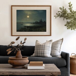 May include: A framed painting of a moonlit scene with a body of water, a boat, and a church in the distance. The painting is hanging on a white wall above a dark gray couch with two pillows.