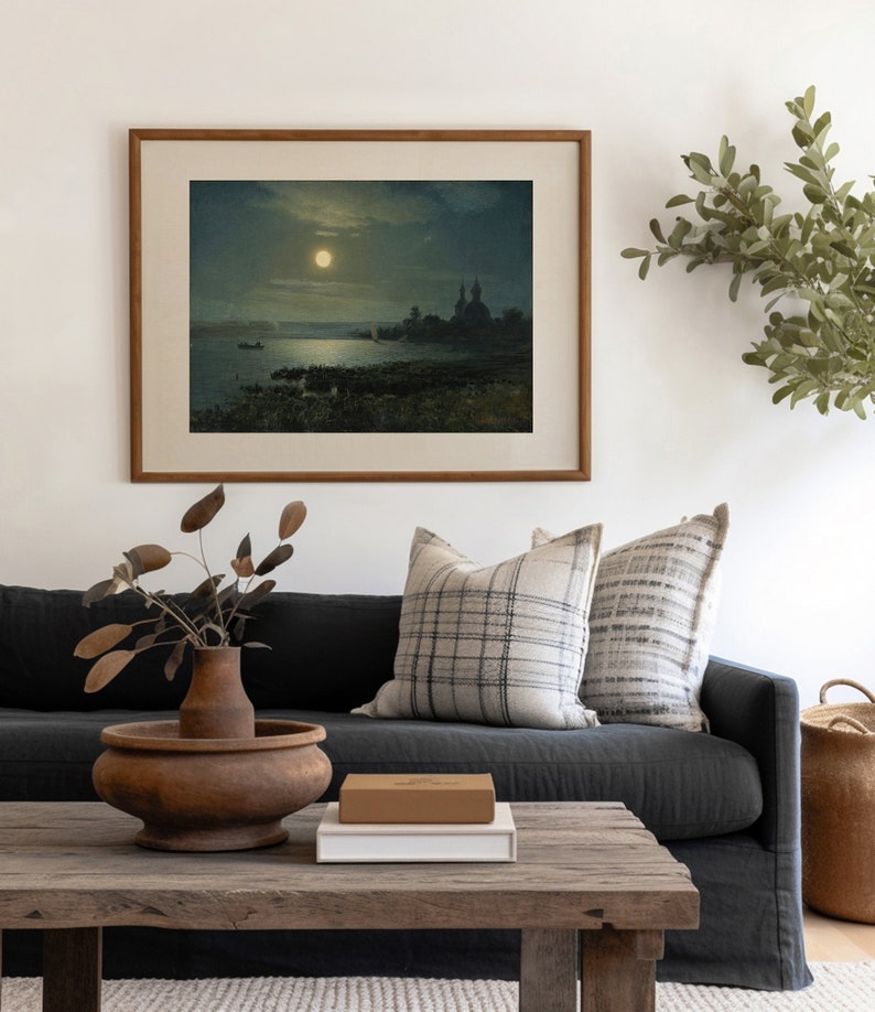May include: A framed painting of a moonlit scene with a body of water, a boat, and a church in the distance. The painting is hanging on a white wall above a dark gray couch with two pillows.