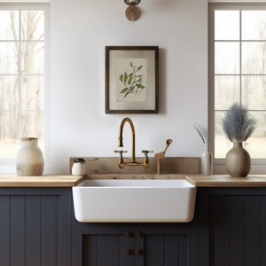 May include: A farmhouse kitchen scene featuring a white apron sink, brass faucet, and framed botanical print. The countertop has a wooden surface, and the cabinets are painted a dark blue. Decorative vases and a small wooden utensil holder add to the rustic charm.