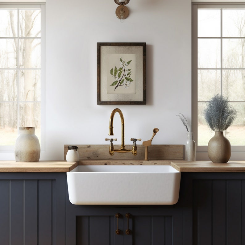 May include: A farmhouse kitchen scene featuring a white apron sink, brass faucet, and framed botanical print. The countertop has a wooden surface, and the cabinets are painted a dark blue. Decorative vases and a small wooden utensil holder add to the rustic charm.