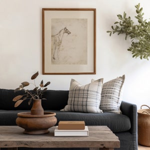 Peut inclure: Un canap&eacute; en lin gris fonc&eacute; avec deux coussins, une table basse en bois avec un vase en c&eacute;ramique brun et un livre sur le dessus, et un dessin encadr&eacute; d'un cheval au mur derri&egrave;re le canap&eacute;.