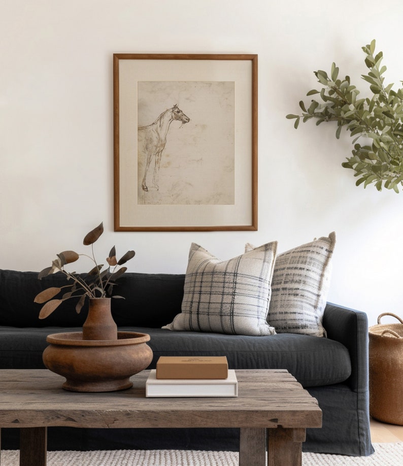 Peut inclure: Un canap&eacute; en lin gris fonc&eacute; avec deux coussins, une table basse en bois avec un vase en c&eacute;ramique brun et un livre sur le dessus, et un dessin encadr&eacute; d'un cheval au mur derri&egrave;re le canap&eacute;.