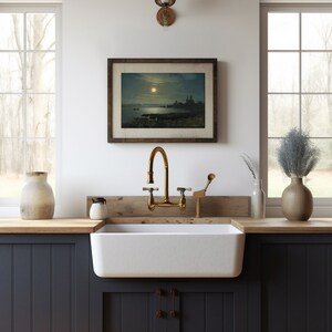 May include: A white farmhouse kitchen sink with a brass faucet and a wooden countertop. A framed picture of a moonlit seascape hangs on the wall above the sink.