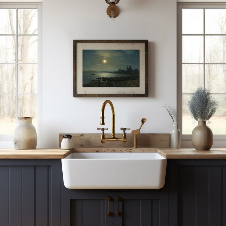 May include: A white farmhouse kitchen sink with a brass faucet and a wooden countertop. A framed picture of a moonlit seascape hangs on the wall above the sink.