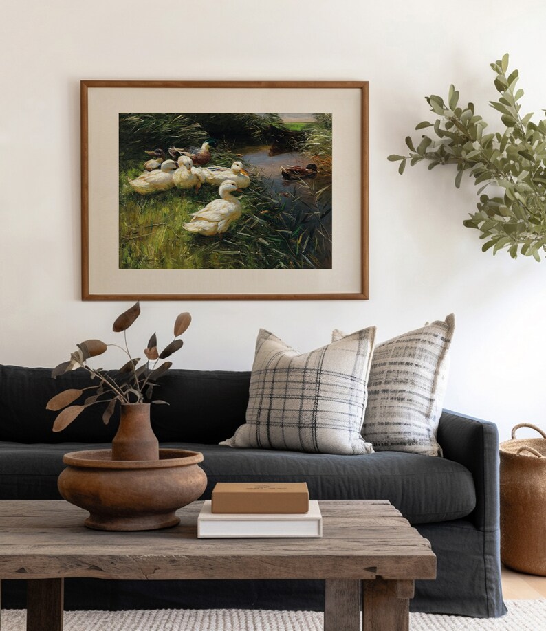 May include: A framed painting of a group of white ducks swimming in a pond with green reeds. The painting is in a wooden frame and is hanging on a white wall.