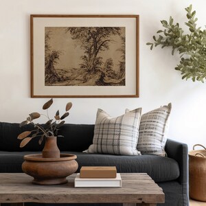 K&ouml;nnte beinhalten: Ein dunkelgraues Sofa mit zwei Kissen, eines mit einem schwarz-wei&szlig; karierten Muster und das andere mit einem grau-wei&szlig; gestreiften Muster. Ein Holz-Couchtisch mit einer braunen Holzkiste und einem wei&szlig;en Buch darauf. Eine Vase mit getrockneten Zweigen steht auf dem Tisch. Ein gerahmtes Schwarzwei&szlig;-Zeichnung einer Landschaft mit B&auml;umen h&auml;ngt an der Wand hinter dem Sofa.