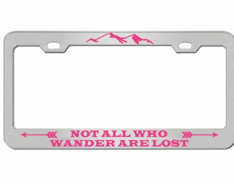 May include: Silver license plate frame with a pink mountain range design and the text "NOT ALL WHO WANDER ARE LOST" with pink arrows on either side.