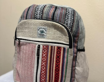 Puede incluir: Una mochila de cáñamo multicolor con un bolsillo frontal y un bolsillo lateral. La mochila presenta una variedad de patrones y colores, incluyendo rayas rojas, blancas y negras. El texto "Himalayan Hemp" es visible.