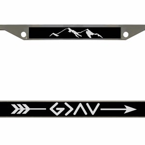 May include: A silver license plate frame with a black background and white mountains and an arrow with the text "G>AV" on the bottom.