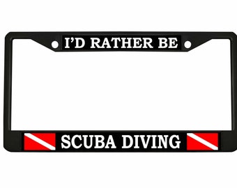 May include: Black metal license plate frame with white text that reads "I'd Rather Be Scuba Diving". The frame has a red and white scuba diving flag on each side.