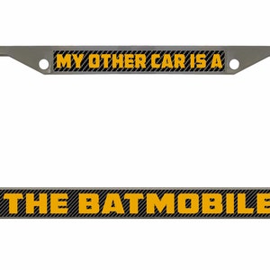 May include: A silver license plate frame with a black and yellow carbon fiber design. The text on the frame reads "My other car is a The Batmobile".