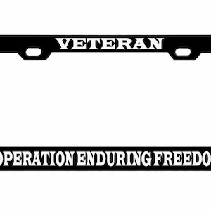 May include: Black license plate frame with the word "VETERAN" at the top and "OPERATION ENDURING FREEDOM" at the bottom in white capital letters. The frame has a rectangular shape with rounded corners and mounting holes.