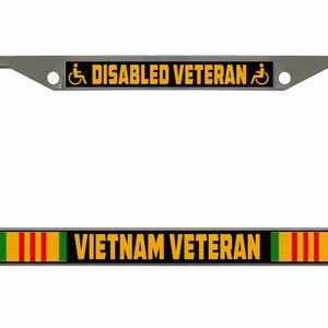 May include: Silver license plate frame with a black and yellow stripe that says "DISABLED VETERAN" with a wheelchair symbol on each side. Below the stripe is another black and yellow stripe that says "VIETNAM VETERAN" with a green, red, and yellow stripe on each side.