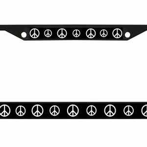 May include: Black metal license plate frame with white peace signs on the top and bottom edges.