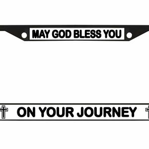 May include: Black license plate frame with white text that reads "MAY GOD BLESS YOU" at the top and "ON YOUR JOURNEY" at the bottom. A cross graphic is on each side of the bottom text.