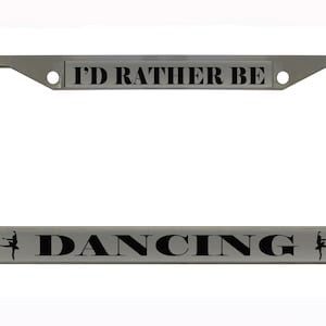 May include: A silver license plate frame with the text "I'D RATHER BE DANCING" in black. The word "DANCING" is centered at the bottom, with a ballerina silhouette on each side.