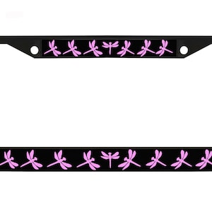 May include: Black license plate frame with a repeating pattern of pink dragonflies on a black background. The frame is rectangular with rounded corners and has two mounting holes.