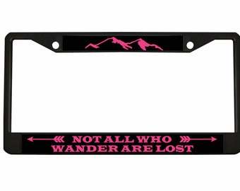 May include: Black metal license plate frame with a pink mountain range design and the text "NOT ALL WHO WANDER ARE LOST" with pink arrows on either side.