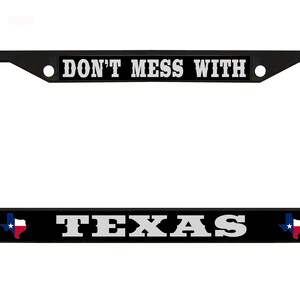 May include: Black metal license plate frame with the text "Don't Mess With Texas" in white lettering. The frame features two small Texas flag graphics on either side of the text.