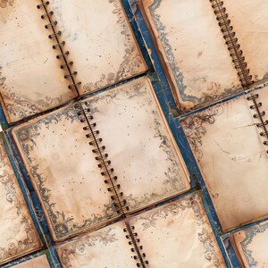 May include: Overhead view of several open spiral-bound notebooks with aged, cream-coloured pages. Each page has a decorative blue and grey floral border. The notebooks are arranged on a blue surface, creating a vintage aesthetic.