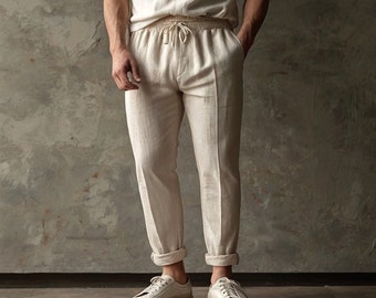 May include: A pair of off-white linen pants with a drawstring waist and cuffed hems. The pants are worn with a white t-shirt and white sneakers.